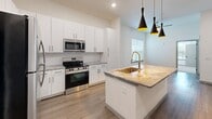 Located at 2775 Drift Ln in Kissimmee, FL, this single-floor residence offers a thoughtfully designed layout that maximizes comfort and functionality. The open-concept kitchen serves as the centerpiece of the home, showcasing a large granite-topped island with an undermount sink and gold-toned faucet, crisp white cabinetry, a herringbone tile backsplash, and a full suite of stainless steel appliances including a range, microwave, refrigerator, and dishwasher. Striking black pendant lights with gold interiors add a modern, upscale touch, while wood-look flooring ties the space together seamlessly. The bedroom is a comfortable retreat featuring plush carpeting, elevated ceilings, and dual windows fitted with blinds that invite ample natural light and views of the surrounding greenery. A dedicated closet provides practical storage. The bathroom is finished with large-format neutral tile surrounding a full soaking tub and shower combination, complemented by wood-look flooring and a granite vanity top. The overall design aesthetic is clean and contemporary, with a neutral color palette, modern hardware, and quality finishes that create a cohesive and inviting living environment.