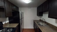Located at 2806 Westbrook St in Kalamazoo, Michigan, this single-floor unit offers a practical and well-organized layout. The kitchen is equipped with dark espresso cabinetry, a stainless steel sink, a black electric range, and a full-size refrigerator, providing ample storage and functionality for everyday cooking. The living area features warm hardwood-style flooring and opens toward the kitchen, creating a connected and open feel. A large sliding glass door fitted with vertical blinds allows natural light to fill the space and provides an exterior view, while a wall-mounted HVAC unit and baseboard heating ensure year-round comfort. The bathroom is notably spacious, featuring a double-sink vanity with a dark countertop, yellow tile wainscoting, tile flooring, and a combined shower and tub enclosure. The bedrooms are carpeted for comfort, each featuring windows with blinds that bring in natural light, along with baseboard heating units. The unit's neutral white walls throughout create a clean, versatile backdrop. The tile ceiling panels and consistent trim work give the space a cohesive, functional character suited for comfortable residential living.