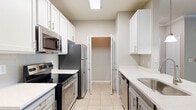 This single-floor residence offers a thoughtfully designed layout with a cohesive, neutral color palette throughout. The galley-style kitchen is a functional highlight, featuring stainless steel appliances including a refrigerator, electric range, over-the-range microwave, and dishwasher. White upper cabinetry pairs with gray lower cabinets and light quartz countertops, while a classic subway tile backsplash adds a clean, modern touch. Light ceramic tile flooring runs throughout the kitchen, which also provides access to a dedicated pantry or storage closet.

The open living area is finished with warm hardwood-style flooring and features crown molding, recessed lighting, and a ceiling fan. A distinctive arched alcove serves as an architectural focal point, and natural light filters in through blinds on nearby windows. The adjoining dining or flex space transitions seamlessly, also benefiting from the crown molding detail.

The carpeted bedroom is generously proportioned, receiving abundant natural light through a large window overlooking lush greenery, and is equipped with a ceiling fan. The bathroom includes a gray vanity with quartz countertop, tile flooring, and direct access to a walk-in closet with built-in shelving. A dedicated laundry room with side-by-side washer and dryer hookups completes this well-rounded space.