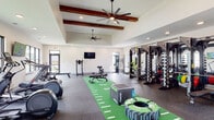 Located at 1630 Lewis Landing Ave in Wilmington, NC, this single-story fitness facility is designed to support a wide range of workout styles and training needs. The main workout area is an expansive, light-filled space anchored by soaring ceilings adorned with rich wooden beams and oversized ceiling fans. Large windows line the perimeter, offering views of the outdoors while flooding the space with natural light. A turf turf turf turf turf turf turf-style functional training runway runs through the center, complemented by a full rack system with cable attachments, free weights, and a variety of cardio equipment including treadmills, ellipticals, and a stationary air bike. Wall-mounted televisions are positioned throughout for entertainment during workouts. A separate studio area features light hardwood-style flooring, floor-to-ceiling mirrors, a wall-mounted TV, built-in open shelving, and spin bikes, making it ideal for group fitness or individual training sessions. The transition corridor connects both zones with textured accent walls, built-in shelving, and a water fountain station. The entryway is welcoming and open, with durable rubber flooring that transitions seamlessly into the main workout spaces. Throughout the facility, the design balances clean, modern aesthetics with warm wood accents, creating an inviting and motivating environment.