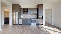 This contemporary single-floor unit offers a thoughtfully designed layout filled with natural light and modern finishes throughout. The standout feature of the living area is its dramatic wraparound corner windows with warm wood framing, allowing sunlight to pour in from multiple angles while framing expansive views of the surrounding cityscape and tree canopy. A ceiling fan with recessed lighting completes the bright, airy atmosphere of this generous open space.

The kitchen is outfitted with dark charcoal cabinetry extending to the ceiling, a tiled backsplash, stainless steel appliances including a refrigerator, range, and built-in microwave, as well as a dishwasher and under-mount sink — offering a clean, functional aesthetic with contemporary appeal.

A secondary bedroom features light hardwood-style flooring, crisp white walls, and a wide horizontal window that frames scenic views of the neighborhood rooftops and surrounding greenery, with a ceiling fan overhead.

Both bathrooms maintain the unit's modern design language, featuring dark wood-toned vanities with under-mount sinks, large mirrors, tiled backsplashes, and full soaking tub-shower combinations. The flooring in both bathrooms is finished in large-format dark tile, providing a grounded contrast to the lighter tones found throughout the rest of the unit.