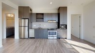 This contemporary single-floor unit offers a thoughtfully designed layout filled with natural light and modern finishes throughout. The standout feature of the living area is its dramatic wraparound corner windows with warm wood framing, allowing sunlight to pour in from multiple angles while framing expansive views of the surrounding cityscape and tree canopy. A ceiling fan with recessed lighting completes the bright, airy atmosphere of this generous open space.

The kitchen is outfitted with dark charcoal cabinetry extending to the ceiling, a tiled backsplash, stainless steel appliances including a refrigerator, range, and built-in microwave, as well as a dishwasher and under-mount sink — offering a clean, functional aesthetic with contemporary appeal.

A secondary bedroom features light hardwood-style flooring, crisp white walls, and a wide horizontal window that frames scenic views of the neighborhood rooftops and surrounding greenery, with a ceiling fan overhead.

Both bathrooms maintain the unit's modern design language, featuring dark wood-toned vanities with under-mount sinks, large mirrors, tiled backsplashes, and full soaking tub-shower combinations. The flooring in both bathrooms is finished in large-format dark tile, providing a grounded contrast to the lighter tones found throughout the rest of the unit.