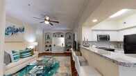 This single-story residence offers a thoughtfully designed layout with cohesive, neutral-toned interiors accented by teal décor throughout. The open-concept living room features hardwood flooring, crown molding, a ceiling fan, and a built-in shelving unit with arched details — providing both storage and a distinctive architectural focal point. A glass-topped coffee table and an abstract area rug anchor the space, which flows directly into the kitchen via a granite-topped breakfast bar with seating.

The kitchen is well-equipped with white cabinetry, granite countertops, a tile backsplash, stainless steel appliances, and hardwood flooring. Adjacent to the living area, the dining space accommodates a round glass table beneath a pendant light fixture, with natural light entering through large windows with plantation-style blinds.

Both bedrooms are carpeted and include crown molding, ceiling fans, and windows that allow ample natural light. The primary bathroom features an extended dual-vanity with white cabinetry, brushed nickel hardware, and tile flooring. A second full bathroom includes a tub-shower combination and matching tile flooring, maintaining a consistent, clean aesthetic throughout the home.