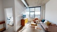Located at 4557 N Sheridan Rd in Chicago's Uptown neighborhood, this single-floor unit showcases an industrial-chic aesthetic defined by exposed concrete ceilings, visible ductwork, and raw structural columns that lend an authentic loft character throughout the space.

The living area is a standout, anchored by a large grid-pane window that frames sweeping views of the Chicago skyline and surrounding cityscape. Natural light floods the room, highlighting the warm-toned hardwood flooring that runs throughout. The open layout comfortably accommodates a seating area and media setup, creating a functional yet stylish living environment.

The bedroom continues the industrial aesthetic, with an exposed concrete column serving as an architectural focal point beside a window that offers additional city views, filling the room with natural light.

The kitchen is designed for practicality and style, featuring two-tone cabinetry — white upper cabinets paired with gray lower cabinets — white quartz countertops, a subway tile backsplash, and a full suite of stainless steel appliances including a gas range and French door refrigerator.

The bathroom is clean and contemporary, with large-format floor tiles, a full tub-shower combination with white tile surround, and a modern vanity with a light stone countertop.