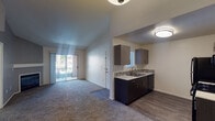 This single-floor residence offers a thoughtfully designed open-concept layout that seamlessly connects the living area and kitchen. The living room features plush carpeting and vaulted ceilings that lend a sense of spaciousness, with a sliding glass door opening to a private balcony that brings in abundant natural light and outdoor views. The kitchen is well-equipped with dark cabinetry, light quartz-style countertops, a mosaic tile backsplash, a double-basin sink, and a full suite of black appliances including a gas range, microwave, dishwasher, and refrigerator. Wood-look flooring runs throughout the kitchen, providing a clean contrast to the carpeted living spaces. The bedroom is generously sized, featuring soft carpeting, a ceiling fan with light fixture, and a window that allows natural light to filter in. The bathroom is finished with modern touches, including a dark wood vanity, white countertop, large wall mirror with overhead lighting, chrome fixtures, and wood-look flooring. Throughout the residence, a neutral color palette and clean lines create a calm and inviting ambiance, while multiple doors provide convenient access and privacy between living areas.