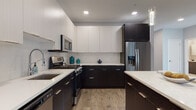 This contemporary single-floor residence showcases a thoughtfully designed open-concept layout with high-end finishes throughout. The kitchen is a standout feature, boasting a striking two-tone design with dark espresso lower cabinets and crisp white upper cabinetry, complemented by quartz countertops, a full suite of stainless steel appliances, and light wood-tone flooring. A central island with bar seating and elegant pendant lighting makes the kitchen equally functional and stylish, flowing seamlessly into the living and dining areas.

The living room is bright and welcoming, benefiting from natural light through large windows. Neutral gray walls and wood-tone flooring create a warm, cohesive aesthetic throughout the common areas.

The bedroom is a serene retreat, featuring the same warm hardwood-style flooring, soft gray walls, and ample natural light that lends a calm, restful ambiance.

The bathroom is finished with large-format light tile flooring, a dark-cabinetry double vanity topped with white quartz counters, dual mirrored medicine cabinets, and a full tub-shower combination clad in classic white subway tile. Every room reflects a consistent modern design language, balancing clean lines with warm, livable finishes.
