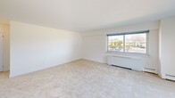 Located at 385 Ocean Blvd in Long Branch, NJ, this one-bedroom, one-bathroom unit offers a practical and comfortable single-floor layout. The galley-style kitchen is well-equipped with warm honey-toned wood cabinetry, dark granite countertops, a gas range, and a full-size refrigerator. Light-colored ceramic tile flooring runs throughout the kitchen, which also features a window that brings in natural light and a view of the surrounding neighborhood. The living area is generously proportioned, finished with neutral carpeting and bright white walls that create a clean, open feel. A large window with blinds allows ample natural light to flow in, and a baseboard heating unit ensures year-round comfort. The spacious primary bedroom continues the carpeted flooring and includes a double-door closet, offering solid storage capacity. The bathroom is thoughtfully finished with full-wall beige ceramic tile, accented by decorative mosaic border strips. A soaking tub with an overhead shower, corner shelf, and grab bar complete the well-appointed space. Overall, the unit presents a tidy, functional layout suited for comfortable everyday living in a coastal New Jersey location.