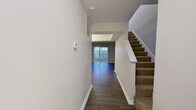 This two-story residence offers a well-organized layout across two floors, combining functional design with practical living spaces. Dark hardwood-style flooring runs consistently throughout the main level, creating a cohesive and polished aesthetic.

The ground floor opens through a hallway that leads past a carpeted staircase into the living room, which serves as the central gathering space. A wood-burning fireplace with a white mantel anchors one wall, while a sliding glass door on the opposite end floods the room with natural light and provides direct access to an outdoor area. The galley-style kitchen is outfitted with dark cabinetry, stainless steel hardware, a mosaic tile backsplash, light countertops, and black appliances, offering efficient use of the available space.

Upstairs, the two bedrooms are finished with dark hardwood-style flooring and ceiling fans. The spacious primary bedroom includes an open closet with double hanging rods and direct access to a private bathroom featuring dark vanity cabinetry. The second bedroom includes a double-door closet for generous storage. Three bathrooms in total serve the home. Neutral wall tones throughout both floors contribute to a clean, understated ambiance.