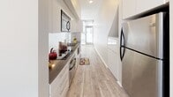 Unit #125 at The Cosmopolitan on Hancock Street offers a thoughtfully designed single-story layout in San Diego. The floor plan, as seen in the 3D model, includes a well-proportioned living area, kitchen, bedroom, and bathroom arranged for functional flow throughout the space.

The kitchen is a standout feature, finished with sleek white cabinetry, dark countertops, and light wood-style flooring. Stainless steel appliances—including a refrigerator, microwave, and oven—provide a modern, cohesive aesthetic. Natural light filters in through large windows at the end of the kitchen corridor, creating a bright and welcoming atmosphere.

The bedroom is finished with neutral carpet and crisp white walls, contributing to a clean and airy feel. Mirrored sliding closet doors add depth to the room while maximizing storage. A ceiling fan provides additional comfort and airflow.

The bathroom presents a striking design contrast, featuring vibrant teal mosaic tile on a full accent wall paired with white tile flooring and clean white fixtures. Recessed lighting and a wall-mounted mirror complete the contemporary look. Overall, the unit maintains a modern, minimalist character throughout.