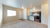 This 2-floor space offers a practical and modern layout with an open-concept main living area that seamlessly connects the living room and kitchen. The living room features neutral-toned carpet, light gray walls, and a window that allows natural light to fill the space, creating a bright and welcoming atmosphere. A flush-mount ceiling light provides additional illumination.

The kitchen is positioned adjacent to the living area and is defined by a raised breakfast bar that serves as a natural divider between the two spaces. Dark espresso cabinetry lines the kitchen walls, complemented by a stainless steel range and microwave, a dark dishwasher, and a sink along the back wall. Pendant lighting hangs above the breakfast bar, adding a refined touch to the functional cooking space.

Dark wood-style flooring runs through the kitchen and entry areas, providing a clean contrast to the carpeted living room. A closet near the entryway offers convenient storage, and a white-paneled entry door completes the main level. The overall design balances practicality with contemporary style, making efficient use of the available space across both floors.