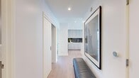 This thoughtfully designed residence offers two bedrooms and two bathrooms across a single floor of well-utilized living space. The open-plan kitchen and living area serves as the heart of the home, where floor-to-ceiling windows frame sweeping panoramic city skyline views, flooding the space with natural light. The kitchen is outfitted with light grey shaker-style cabinetry extending to the ceiling, a bold dark subway tile backsplash, white quartz countertops, stainless steel appliances, and light hardwood flooring that continues throughout the unit.

A welcoming hallway connects the living areas to the private quarters, with a stylish upholstered bench and curated artwork setting an elevated tone. The spacious primary bedroom features large windows with city views and access to a dedicated closet. Its en-suite bathroom includes a floating vanity, glass-enclosed walk-in shower with dark stone tile, and pendant lighting. The second bedroom also includes an organized walk-in closet. The second bathroom offers a soaking tub, floating vanity, and refined pendant fixtures. Clean white walls and hardwood floors create a cohesive, modern aesthetic throughout.