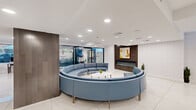 Located at 4247 Locust Street in Philadelphia's University City neighborhood, this contemporary amenity space is thoughtfully designed across a single floor. The layout is divided into two primary areas: a welcoming lounge and a dedicated fitness center.

The lounge area makes an immediate impression with its striking circular blue sectional sofa centered around a round white coffee table, creating an inviting, social atmosphere. Polished large-format white tile flooring reflects the recessed lighting overhead, lending the space a bright and airy quality. A wall-mounted fireplace with a wood-panel surround and modern artwork anchors one wall, while floor-to-ceiling glass partitions provide visual connectivity throughout. Dark wood accent columns add warmth and contrast against the crisp white walls and ceilings.

The fitness center is well-appointed with a broad selection of cardio equipment, including treadmills, ellipticals, and stationary bikes, alongside free weights, a weight bench, and exercise balls. Rubber flooring, recessed lighting, and street-facing windows provide a functional yet energizing environment. An inspirational typographic mural adds a motivating aesthetic touch to the workout space.

A transitional entry area features glossy white tile, glass-walled access points, and a small workstation, providing a clean and organized threshold between areas. Together, these spaces offer a polished, modern amenity experience.