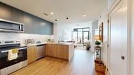 Located at 4098 Hillsboro Pike in Nashville, TN, this well-designed one-bedroom, one-bathroom residence offers a thoughtfully arranged open-concept layout across a single floor. Light wood flooring flows throughout, creating a warm and cohesive aesthetic.

The kitchen is a standout feature, showcasing dual-tone cabinetry with slate-blue upper cabinets and natural wood lower cabinets, complemented by a marble-style backsplash, white quartz countertops, and stainless steel appliances. The peninsula provides additional prep space and opens seamlessly into the living area.

The living room is anchored by dramatic floor-to-ceiling windows that flood the space with natural light and frame expansive outdoor views of the Nashville skyline and surrounding neighborhood. Access to a private balcony further extends the living space.

The bedroom offers a tranquil retreat, also benefiting from oversized windows with scenic views, providing a bright and airy atmosphere. A dedicated closet offers ample storage.

The bathroom is elegantly finished with a wood-toned vanity, white countertops, a large mirror, tile flooring, and a glass-enclosed shower. Clean white walls and crisp fixtures complete the refined look throughout this modern Nashville residence.
