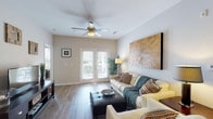 Located at 327 Guinevere Ln in Wilmington, NC, this single-story residence offers a well-designed layout with comfortable living spaces throughout. The living room is bright and welcoming, featuring wood-look plank flooring, neutral walls, a ceiling fan, and French doors that open to a private balcony, allowing natural light to fill the space. A large wood-panel wall accent adds a warm, artistic focal point to the room. The kitchen is equipped with warm oak cabinetry, granite countertops, and black appliances including a range, microwave, and refrigerator. A dedicated in-unit laundry area is conveniently accessible from the kitchen. Adjacent to the kitchen is a cozy dining nook with wood-look flooring, ideal for casual meals. The residence includes two bedrooms, each carpeted and outfitted with ceiling fans and windows that bring in natural light. Both bathrooms feature granite-topped vanities, oak cabinetry, tub-shower combinations, and wood-look flooring. The primary bathroom includes access to a walk-in closet with built-in shelving. Overall, the home presents a clean, neutral palette with consistent finishes that create a cohesive and comfortable living environment.