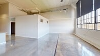 Located at 424 Memorial Dr in Danville, Virginia, this 2-bedroom, 1-bathroom unit showcases a distinctive industrial aesthetic with thoughtful modern finishes throughout. The open-concept living, dining, and kitchen area is the heart of the home, boasting soaring ceilings with exposed ductwork, polished concrete floors, and dramatic factory-style windows that flood the space with natural light and offer sweeping outdoor views. The kitchen features a large granite-topped island with a double sink, stainless steel appliances including a refrigerator, range, and microwave, and gray cabinetry — all beneath striking pendant lighting. The generously sized living area benefits from the lofty ceiling height, creating an airy, loft-like ambiance. Both bedrooms continue the polished concrete flooring and are served by two closets for ample storage. The primary bedroom features elevated ceilings and a walk-in closet. The full bathroom includes a dark-cabinetry vanity with granite countertop and a tub-shower combination. A dedicated laundry room with a full-size washer and dryer adds everyday convenience. Hallways connect all areas efficiently, completing this well-appointed, industrial-modern residence.
