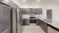 Located at 4209 Brett Ave in Sioux Falls, South Dakota, this single-floor unit offers a clean, modern aesthetic with thoughtfully selected finishes throughout. The kitchen is a standout feature, equipped with rich dark-toned shaker-style cabinetry, granite countertops, a large kitchen island with an undermount sink, and a full suite of stainless steel appliances including a refrigerator, range, and over-the-range microwave. Light wood-look flooring ties the kitchen and living areas together seamlessly. The open living area is bright and airy, benefiting from recessed lighting and a sliding glass door that opens to a private balcony, bringing in natural light and views of the surrounding neighborhood. The bedrooms are finished with plush carpet flooring and neutral wall tones, creating comfortable and versatile spaces. One bedroom features a walk-in closet outfitted with wire shelving for ample storage. The bathroom continues the cohesive design language with matching dark cabinetry, granite countertops, and a built-in linen tower for added storage. Throughout the unit, clean lines, neutral tones, and quality materials come together to create a polished and inviting living environment.
