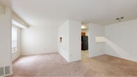 This single-floor unit offers three bedrooms and one bathroom within a efficiently organized layout. The living area is the most prominent shared space, featuring wall-to-wall carpeting in a neutral tone and a large sliding glass door fitted with vertical blinds, allowing natural light to fill the room and providing outdoor access. A secondary window on an adjacent wall further brightens the space. The living area connects to a partitioned wall that separates it from the kitchen, which features light wood-style flooring, warm-toned wood cabinetry, a black refrigerator, and a pass-through countertop ledge that opens toward the main living space.

The three bedrooms are carpeted and finished in neutral white and beige tones, each with standard windows that admit natural light. The primary bedroom offers a generous footprint among the three. The single bathroom includes a full-sized soaking tub with a white surround enclosure and chrome fixtures. Throughout the unit, the consistent use of light wall colors, neutral carpeting, and simple finishes creates a clean, functional ambiance suited for everyday living.