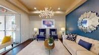 Located at 10 W Minnezona Ave in Phoenix, AZ, this thoughtfully designed community space delivers a vibrant and welcoming atmosphere across a single, open floor. The layout flows seamlessly from a glass-door entrance — adorned with framed butterfly artwork — into distinct functional zones that balance style with practicality.

The lounge area anchors the space with a coffered, gold-toned ceiling and a dramatic white antler chandelier as its centerpiece. Bold cobalt blue accent walls create a striking contrast against neutral tones, while a tufted cream sofa, pair of royal blue wingback chairs, and a starburst mirror contribute to the space's eclectic yet cohesive design. Dark hardwood-style flooring runs throughout, grounding the interior.

A large granite-topped bar island with seating serves as a social hub, complemented by pendant lighting, dark cabinetry, and a wall-mounted television set against a deep blue backdrop — ideal for gatherings or casual use.

Adjacent to the bar, a bright and airy dining area features floor-to-ceiling windows and elegant patterned drapes, flooding the room with natural light and offering views of palm trees and the surrounding Phoenix landscape. A ceiling fan and mixed seating — including bar-height tables and a central round dining table — provide versatile options for residents or visitors. The overall ambiance is modern, inviting, and carefully curated.