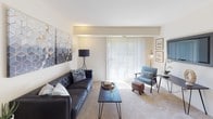This single-floor residence offers a thoughtfully arranged layout with a comfortable mix of living, dining, and sleeping spaces. The living room serves as the central gathering area, featuring plush carpeting, a large sliding glass door that invites an abundance of natural light, and vertical blinds that offer privacy when needed. The space is well-proportioned and versatile, easily accommodating a seating arrangement anchored by a tufted sofa and accent chair.

The kitchen is efficiently designed with light wood cabinetry, dark countertops, and white appliances, including a range, microwave, and dishwasher. A window above the sink brings in natural light, enhancing the functional workspace. Adjacent to the kitchen, the dining area provides a dedicated space for meals, complete with a modern pendant light fixture and a round wall mirror that adds depth to the room.

Both bedrooms are carpeted and bathed in natural light from multiple windows with blinds. The rooms offer ample space for full bedroom furniture sets and feature neutral wall tones that create a calm, restful atmosphere.

The bathroom includes classic mosaic tile flooring, a light wood vanity with an integrated sink, and a full bathtub with tiled surround, offering a clean and practical design throughout.