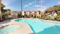 This vibrant residential community is designed with an array of outdoor amenities that cater to a variety of lifestyles. At the heart of the grounds lies a generously sized, freeform swimming pool with crystal-clear water, accompanied by an adjacent spa. The pool deck is outfitted with lounge chairs and shaded patio seating beneath orange market umbrellas, creating a relaxed, resort-like atmosphere. Towering palm trees frame the surroundings, adding to the sun-soaked ambiance.

A dedicated outdoor BBQ area features a built-in stainless steel grill set on a stone base, covered by a modern pergola with shade canopy. A winding walkway leads through manicured green lawns, connecting the various amenity spaces across the property.

Younger residents are well served by a fully equipped playground situated on a rubberized safety surface beneath a canopy of mature shade trees. Sports enthusiasts will appreciate the full basketball court, enclosed by chain-link fencing and surrounded by lush greenery and palms.

Pet owners will find a thoughtfully designed dog park featuring artificial turf, agility equipment, pergola-shaded seating, and secure fencing — offering a safe and enjoyable space for four-legged residents. The multi-building community reflects a consistent architectural style with red tile roofing, balconies, and well-maintained landscaping throughout.