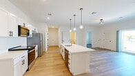 Located at 3883 East Market Street in York, PA, this thoughtfully designed 2-bedroom, 2-bathroom residence offers a clean, modern aesthetic throughout its single-floor layout. The open-concept kitchen and living area serves as the heart of the home, anchored by a large white kitchen island with a built-in sink and pendant globe lighting overhead. White shaker-style cabinetry, stainless steel appliances — including a refrigerator, range, and microwave — and light wood-look flooring create a bright, cohesive atmosphere. The living area flows naturally from the kitchen, offering generous space for everyday living. Both bedrooms feature soft carpeting and ample closet space, with one bedroom providing direct access to the patio via sliding glass doors — ideal for enjoying outdoor views. Five closets are distributed throughout the unit, offering exceptional storage. The two bathrooms are finished in a clean, contemporary style with white vanity cabinetry, light wood flooring, and modern fixtures; one features a walk-in shower with grab bars, while the other includes a full tub-shower combination. A dedicated laundry area adds everyday convenience. The overall palette of crisp whites and warm wood tones gives the space a fresh, move-in-ready feel.