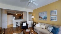 Located at 612 Council St in Wilmington, NC, this single-story home offers a thoughtfully designed layout that blends comfort and functionality. The living area is a welcoming focal point, featuring warm hardwood floors, a ceiling fan, and a bold accent wall painted in a rich golden yellow that adds character and warmth to the space. A piece of abstract wall art enhances the contemporary aesthetic. The open-concept design connects the living room seamlessly to the kitchen, which is visible through a pass-through opening framed by a breakfast bar with industrial-style stools — ideal for casual dining or entertaining. The kitchen is equipped with dark wood cabinetry, stainless steel appliances including a microwave and range, and track lighting that illuminates the workspace effectively. A pendant light adds a refined touch above the counter. Throughout the home, natural light filters in, contributing to a bright and airy ambiance. The layout is efficient and functional, making excellent use of the available space. The combination of warm tones, modern fixtures, and an open flow creates an inviting atmosphere well-suited for everyday living.