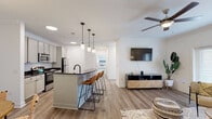 Located at 5632 Tierra Roja Dr in Virginia Beach, Virginia, this single-floor residence presents a clean, contemporary design with a cohesive aesthetic carried throughout each room. The open-concept living and kitchen area serves as the heart of the home, where wood-look plank flooring, crown molding, and crisp white walls create a bright, welcoming atmosphere. A ceiling fan overhead complements the natural light that filters in through French doors leading to the outdoors.

The kitchen is thoughtfully designed with gray cabinetry, dark countertops, a geometric tile backsplash, and stainless steel appliances. A central island with a matte black faucet and pendant lighting above provides convenient bar seating, seamlessly connecting the kitchen to the living space. Adjacent to the kitchen, a dedicated dining area features crown molding and a pendant chandelier overhead.

The bedrooms offer a comfortable retreat, with plush carpet flooring, ceiling fans, and generous windows that invite natural light. The primary bedroom connects to a well-finished bathroom featuring a vanity with dark countertops, tile flooring, and a glass-enclosed walk-in shower. A dedicated laundry room with a full-size washer and dryer adds notable everyday convenience to this well-rounded home.