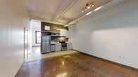 Located in the heart of Downtown Los Angeles on South Broadway, this single-floor urban unit blends industrial character with modern functionality. The open-plan main area features polished concrete floors that reflect light throughout the space, creating a sleek, contemporary feel. Soaring ceilings with exposed structural beams, visible ductwork, and track lighting reinforce the loft-inspired aesthetic while providing an airy, expansive atmosphere. Large glass entry doors allow natural light to filter into the living area, enhancing the sense of openness.

The kitchen is fully equipped with stainless steel appliances, including a refrigerator, electric range, dishwasher, and microwave. White cabinetry and clean countertops provide ample storage and prep space, while a distinctive geometric-patterned tile floor delineates the kitchen zone from the polished concrete of the main living area, adding a classic design accent.

The bathroom continues the industrial-modern theme, featuring large-format flooring tiles, a floating white vanity, full-size soaking tub, and floor-to-ceiling vertical tile in the wet area. The overall design of the space offers a versatile, open canvas well-suited for a variety of uses in one of Los Angeles's most vibrant urban neighborhoods.
