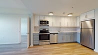 Located at 107 Sunderland Rd in Amherst, Massachusetts, this well-designed single-floor residence offers a clean, modern aesthetic throughout. Light wood-tone flooring runs continuously across the living, dining, and bedroom areas, creating a cohesive and inviting atmosphere.

The kitchen is a standout feature, outfitted with a full suite of stainless steel appliances including a range, built-in microwave, dishwasher, and refrigerator. Two-tone cabinetry — white upper cabinets paired with soft grey lower cabinets — is complemented by a marble-style tile backsplash and light quartz countertops, giving the space a polished, contemporary look. Flush-mount ceiling lighting adds a modern finishing touch.

The open living area flows naturally from the kitchen, offering a generous, flexible layout. Bedrooms are bright and well-proportioned, with large windows that bring in abundant natural light and offer views of the surrounding greenery.

Two bathrooms serve the unit. The primary bathroom features large-format wood-look floor tiles, a white vanity with a quartz countertop, backlit mirrors, and a separate shower. The secondary bathroom is finished with neutral tile flooring and includes a full soaking tub with shower. Both bathrooms maintain a clean, minimalist design consistent with the rest of the residence.