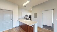 Located at 430 E Elm St in Springfield, MO, this 1-bedroom, 2-bathroom unit offers a thoughtfully designed single-floor layout that maximizes functionality and comfort. The open-concept kitchen, dining, and living area serves as the heart of the space, anchored by a granite-topped peninsula with an undermount sink and rich wood cabinetry. The kitchen is fully equipped with stainless steel appliances, including a range, over-the-range microwave, and refrigerator, complemented by white upper cabinetry and matching granite countertops. Wood-look flooring runs throughout the main living areas, while a stylish multi-pendant chandelier adds a warm focal point above the dining area. A sliding glass door floods the living space with natural light and opens to a private balcony with views of the surrounding greenery. The bedroom features plush carpeting, a closet, and a bright window overlooking the outdoors. Two bathrooms offer granite-topped vanities with white cabinetry, providing ample storage. Additional conveniences include a dedicated laundry area and utility room. The overall aesthetic is clean and contemporary, with neutral tones and modern finishes throughout.