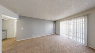 Located at 3955 E Charleston Blvd in Las Vegas, NV, this single-floor unit offers a practical and well-organized layout across two bedrooms, two bathrooms, a living room, kitchen, hallway, and two closets. The living room is a comfortable, open space featuring soft carpet flooring, neutral gray walls, a textured ceiling, and a sliding glass door fitted with vertical blinds that allows natural light to fill the room and provides access to the outdoors. The kitchen is efficiently designed with gray cabinetry, speckled stone countertops, tile flooring, a white appliance suite including a range and refrigerator, and a peninsula counter that doubles as a casual dining or prep area. An adjacent dining nook benefits from a ceiling fan and a window with vertical blinds. The primary bedroom is a generously sized carpeted room with white walls, a textured ceiling, and a window that brings in natural light. The second bedroom mirrors this clean, neutral aesthetic with carpet flooring and its own window. Both bathrooms feature tile flooring and tub-shower combinations with clean white finishes. Throughout the unit, a consistent palette of whites and neutrals creates a bright, functional living environment.
