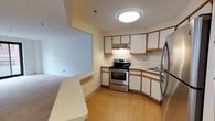 This single-floor residence offers a practical and comfortable layout designed for efficient everyday living. The kitchen is a standout feature, equipped with stainless steel appliances including a range and refrigerator. White cabinetry with warm wood-tone trim lines the walls, providing ample storage space, while light wood-style flooring adds a clean, cohesive aesthetic throughout. A built-in counter peninsula connects the kitchen to the adjacent living area, creating a natural transition between spaces and offering additional workspace or casual dining potential. The kitchen also features an under-cabinet range hood and a dedicated sink area, making it both functional and well-organized. The living area is finished with neutral-toned carpet, contributing to a warm and inviting atmosphere. Soft, warm wall tones throughout the residence create a calm and welcoming ambiance. Flush ceiling lighting ensures the space is well-illuminated. The single-bedroom, one-bathroom configuration makes this residence an ideal choice for individuals or couples seeking a manageable, thoughtfully designed living space on one convenient level.
