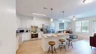 Located at 7300 Ashlake Pkwy in Chesterfield, VA, this single-story, 2-bedroom, 2-bathroom residence offers a thoughtfully designed layout with modern finishes throughout. The open-concept kitchen and living area serves as the heart of the home, anchored by a large granite-topped island with bar seating and pendant lighting overhead. The kitchen is outfitted with crisp white shaker cabinetry, stainless steel appliances including a French door refrigerator and electric range, and light hardwood-style flooring that extends throughout the main living areas. The living room receives generous natural light through large windows with views of the surrounding greenery. Both bedrooms feature plush carpeting and ceiling fans, with the primary bedroom offering a bright window with outdoor views. The second bedroom is spacious and includes a walk-in closet. The two bathrooms are finished with granite vanities and tile flooring; one includes an accessible roll-in shower with grab bars. Additional highlights include four closets providing ample storage, a dedicated laundry area, and a walk-in closet with wire shelving. The residence combines accessibility-conscious design with contemporary style, creating a comfortable and functional living environment.