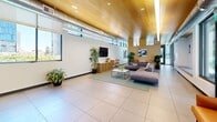 Located at 2345 Waverly St in Oakland, CA, this single-floor community space offers a thoughtfully designed open-plan layout encompassing a living room, dining area, and a fully equipped kitchen. The interior is defined by soaring ceilings clad in warm wood paneling, exposed industrial-style ductwork, and large-format tile flooring that runs throughout, lending the space a contemporary yet welcoming character.

The living room is generously proportioned, featuring a sectional sofa arrangement centered on a coffee table, curated indoor plants, and wall-mounted artwork. Floor-to-ceiling windows and glass doors flood the area with natural light while offering views of the landscaped outdoor surroundings.

The kitchen is a standout feature, outfitted with stainless steel appliances, a sleek range with hood, a striking iridescent mosaic tile backsplash, and an expansive white quartz island with built-in sink and bar seating for multiple guests. Pendant lighting and direct outdoor access via sliding glass doors enhance both function and atmosphere.

The dining area provides a more intimate setting with booth-style seating upholstered in grey fabric, arranged around a central white table beneath exposed ceiling elements. Additional seating nooks with leather accent chairs and small work tables offer flexible use throughout the space, making it ideal for gathering, dining, or casual collaboration.