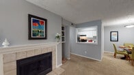 Located at 500 Bridle Ridge Ln in Raleigh, NC, this single-floor residence offers a well-organized layout with thoughtfully designed living spaces throughout. The living room serves as the heart of the home, anchored by a tile-surround fireplace flanked by built-in shelving on both sides — ideal for display and storage. Neutral gray walls and plush carpeting create a warm, cohesive atmosphere, while a pass-through window connects the living area directly to the kitchen, enhancing the open feel. The kitchen is equipped with white shaker-style cabinetry, clean white countertops, and black appliances including a gas range with overhead ventilation. A separate dining or flex area with sliding glass doors opens onto a covered patio, offering a seamless transition to the outdoors and views of mature surrounding trees. The bedrooms feature carpeted floors, large windows that invite natural light, and textured ceilings. One bedroom includes a built-in wall shelf, adding a practical architectural detail. The bathroom is finished with wood-look flooring and a tub-shower combination. Throughout the home, the consistent gray color palette and carpeted flooring lend a unified, comfortable character well-suited to everyday living.
