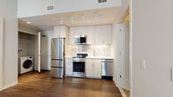 This well-appointed single-floor unit offers a thoughtfully designed layout that maximizes functionality and modern aesthetics throughout. The kitchen is a standout feature, showcasing floor-to-ceiling light-toned cabinetry, a full suite of stainless steel appliances including a French-door refrigerator, electric range, built-in microwave, and dishwasher. A white subway tile backsplash and under-cabinet lighting add refined detail, while track lighting overhead ensures excellent illumination. Rich, dark hardwood flooring flows seamlessly throughout the main living areas, providing a warm contrast to the bright, neutral walls. The bathroom is finished with a clean, contemporary aesthetic, featuring a wide white quartz vanity with an undermount sink, brushed nickel hardware, tile flooring with a wood-look pattern, and a private water closet. The bedroom benefits from multiple windows fitted with blinds, allowing for abundant natural light and views to the outside, and is complemented by a built-in sliding-door closet. Additional conveniences include in-unit laundry, visible from the 3D overview, and smart entry door hardware. The overall ambiance is clean, modern, and move-in ready.