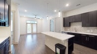 This single-floor residence offers a thoughtfully designed open-concept layout that seamlessly connects the kitchen and living areas. The kitchen is a standout feature, showcasing rich dark cabinetry, a neutral tile backsplash, stainless steel appliances, and a large center island with a white countertop and pendant lighting overhead — ideal for both cooking and casual dining. Wood-look flooring flows throughout the main living areas, lending warmth and continuity to the space.

The living area is bright and welcoming, enhanced by a ceiling fan, recessed lighting, and French doors with transom windows that invite natural light and provide outdoor access. The bedrooms feature plush carpeting and windows with blinds, creating a comfortable and quiet retreat. One bedroom also benefits from its own set of French doors.

The primary bathroom is well-appointed, featuring a double-sink vanity with dark cabinetry and white countertops, large-format tile flooring, a glass-enclosed shower with decorative tile accents, and a soaking tub. A walk-in closet with built-in shelving connects directly to the bathroom, providing generous storage. The overall aesthetic throughout is clean and contemporary, with a consistent palette of dark fixtures against light walls and surfaces.
