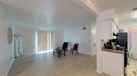 This single-floor residence offers a thoughtfully designed layout that balances open communal spaces with functional private areas. The living room is bright and airy, featuring light wood-style flooring, crisp white walls, and a large sliding glass door dressed with vertical blinds that floods the space with natural light. The open floor plan allows the living area to flow seamlessly into the dining space, which is equipped with a ceiling fan for added comfort.

Adjacent to the living area, the galley-style kitchen is efficiently arranged with white cabinetry, granite-style dark countertops, stainless steel appliances including a refrigerator and dishwasher, and a double sink. A peninsula counter provides a convenient pass-through connection to the main living area. A hallway leads from the living space to the private quarters, maintaining a clear and organized circulation path throughout the residence.

The bedroom is finished with plush carpeting and features a ceiling fan with a light fixture, along with a window that brings in natural light. The bathroom is outfitted with a vanity topped with granite-style countertops, a wide mirror, and white cabinetry, offering a clean and practical design. Throughout the residence, the consistent use of light tones and durable materials creates a cohesive, welcoming atmosphere.