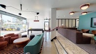 Located at 750 Garland Ave in downtown Los Angeles, this amenity lounge is a thoughtfully designed communal space that blends retro-modern aesthetics with contemporary functionality. The space is characterized by a bold color palette — teal accent walls, deep burgundy furnishings, and vivid red railings — that create a lively and energetic atmosphere throughout.

The layout flows across a single level with distinct zones serving different purposes. A sunken lounge area features plush, curved sofas and accent chairs arranged around low tables, anchored by patterned terrazzo-style flooring and a wall-mounted flat-screen television. Adjacent to this is a coworking and dining area outfitted with long bar-height tables, black stools, and striking multi-arm pendant lighting — ideal for focused work or casual gatherings.

A billiards table anchors the game zone near large floor-to-ceiling windows that flood the space with natural light and offer views of the outdoor pool area. The pool deck, visible through expansive glass doors, extends the living space outdoors with lounge seating along the water.

Polished concrete floors run through the corridors connecting private rooms or meeting spaces, lined with black-framed glass partitions. The overall design is cohesive, energetic, and well-appointed — offering residents a multifunctional social environment in the heart of Los Angeles.