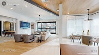Located on Erwin Road in Durham, North Carolina, this single-floor amenity space is thoughtfully designed to accommodate a variety of social and professional needs. The layout flows seamlessly between distinct functional zones, each characterized by contemporary finishes, curated furnishings, and an abundance of natural light.

The main lounge area features warm light wood flooring, crisp white walls, and exposed steel beams that contrast with a striking wood-paneled ceiling. Large floor-to-ceiling black-framed glass doors and windows offer views of the surrounding outdoor spaces, flooding the interior with natural light. A sculptural multi-arm chandelier anchors the seating arrangement, which includes a neutral sofa, upholstered armchairs, and minimalist side tables.

The dining and social area transitions smoothly from the lounge, showcasing sheer floor-length drapery, pendant lighting, and a mix of round and rectangular tables suited for casual gatherings or communal dining. Concrete planter boxes with moss accents add a natural, organic touch.

A dedicated co-working zone provides a conference table, wall-mounted display, and secondary high-top workstations set against a warm wood-paneled accent wall. Enclosed private meeting rooms with glass walls and doors offer a quieter setting for focused work. Throughout, patterned carpeting, carefully selected artwork, and layered lighting contribute to a polished yet welcoming ambiance.