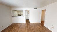 Located at 7000 Red Fox Trail in Shreveport, Louisiana, this single-floor residence offers a practical and functional layout throughout. The main living area is anchored by rich wood-look plank flooring and features a textured ceiling, with natural light streaming in through a sliding glass door flanked by vertical blinds, creating a bright and open atmosphere.

The kitchen is accessed via a pass-through window from the living area, providing an open, connected feel between the spaces. It is equipped with white cabinetry, a dark granite-style countertop, a white electric coil range with an overhead exhaust hood, and a full-size white refrigerator — offering all essential appliances in a compact, efficient layout.

The bedrooms are finished with neutral carpet and feature windows that allow natural light to filter in. One bedroom includes a built-in vanity with a lighted mirror and drawers, adding a functional design element. A dedicated storage room features floor-to-ceiling adjustable shelving and lower cabinet storage, providing ample organization space.

The bathroom includes a white vanity with a dark countertop, an illuminated mirror, and a tub-shower combination, maintaining a clean and functional design consistent throughout the home. Central HVAC vents are present throughout, ensuring year-round climate comfort.