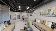 Located at 742 S Westlake Ave in Los Angeles, this single-floor commercial space offers a striking industrial-chic aesthetic that blends raw architectural elements with stylish, functional furnishings. The defining feature of the interior is the dramatically painted black ceiling, which showcases an exposed network of ducts, pipes, and linear LED lighting fixtures — a hallmark of modern industrial design that adds character and visual depth to the open layout.

The polished light-colored concrete floors contrast beautifully against the dark ceiling, creating a bright and airy atmosphere throughout. The expansive open floor plan is divided into distinct functional zones. A comfortable lounge area features neutral-toned sofas and armchairs arranged around a glass-top coffee table, accompanied by decorative plants and layered area rugs that soften the industrial setting. Adjacent to this, a generous dining area accommodates a large farmhouse-style wooden table surrounded by slipcover-draped chairs, ideal for communal gatherings.

A window along one wall allows natural light to filter in, providing a pleasant connection to the surrounding urban environment. Toward the rear of the space, yellow-accented doors lead to restroom facilities, and a kitchenette or bar area with dark cabinetry offers additional utility. Decorative shelving, wall art, and curated accessories throughout add warmth and personality, making this versatile space well-suited for events, meetings, or community use.