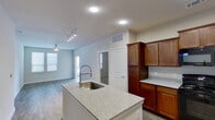 This single-floor residence offers a thoughtfully designed open-concept layout that seamlessly connects the kitchen and living areas. The kitchen serves as the centerpiece of the space, anchored by a white center island topped with light granite countertops and equipped with a professional-style pull-down faucet and stainless steel sink. Rich, warm-toned cabinetry extends from floor to ceiling, providing generous storage, while black appliances — including a refrigerator, range, and over-the-range microwave — complete the functional setup. Hard-surface flooring runs through the kitchen and extends into the adjacent open living area, which is brightened by natural light from multiple windows and features a ceiling fan overhead. A track lighting fixture adds additional illumination to the shared living space. The bedrooms are carpeted for comfort, each featuring neutral walls, window blinds, and ceiling fans, creating calm and restful retreats. The bathroom is finished with wood-look vinyl flooring, a single-sink vanity with warm wood cabinetry, and a full tub and shower combination lined with classic tile surround. Clean white walls and trim throughout lend the space a fresh, move-in-ready aesthetic.