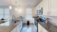 Located on Sansom Street in Philadelphia's West Philadelphia neighborhood, this single-floor, 3-bedroom, 2-bathroom unit offers a well-organized layout designed for comfortable everyday living. The open-concept kitchen and living area form the social heart of the unit. The kitchen is outfitted with white shaker-style cabinetry, dark granite countertops, stainless steel appliances including a French door refrigerator, electric range, and microwave, as well as a double-basin sink beneath pendant lighting. A window with blinds admits natural light, enhancing the clean, modern aesthetic. Wood-style plank flooring runs throughout the main living areas, lending visual continuity. The living room provides a bright, open setting with large windows and straightforward access to the bedrooms via a central hallway. The primary bedroom features a double-door closet and a high horizontal window. Additional bedrooms are simply finished with light walls and wood-style flooring. Both bathrooms include tile flooring, vanities, and shower enclosures with curtains. The overall design is contemporary and neutral, emphasizing functionality and clean finishes throughout.