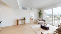Located at 856 Gramercy Dr in Los Angeles, this well-appointed 4-bedroom, 2-bathroom home offers a thoughtfully designed single-floor layout with a clean, modern aesthetic. Light hardwood flooring runs throughout, complementing the bright white walls and recessed lighting that give the entire space an airy, open feel.

The combined kitchen and living area serves as the heart of the home. The kitchen is outfitted with two-tone cabinetry — warm wood lower cabinets paired with soft grey uppers — white quartz countertops, a subway tile backsplash, and a full suite of stainless steel appliances. The adjacent living room is generously proportioned with large sliding glass doors that flood the space with natural light and provide direct access to the balcony.

The private balcony is a standout feature, offering sweeping views of the Los Angeles skyline — an impressive urban backdrop visible from both the living room and the primary bedroom. The primary bedroom is a comfortable retreat with direct balcony access and a dedicated walk-in closet with wrap-around shelving. Sliding mirrored closet doors add a refined touch to the additional bedrooms.

Both bathrooms feature light wood vanities, white countertops, and full shower-tub combinations with clean tile surrounds. A hallway connects all rooms, and the overall layout ensures a functional flow throughout the home.
