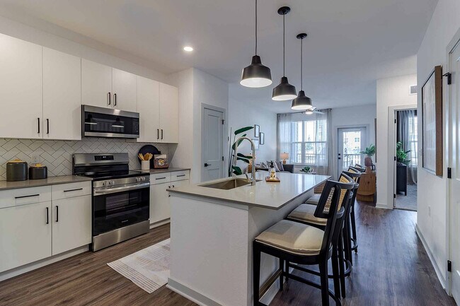 Cocine y reúnase en la cocina de concepto abierto del plano de planta A1, que cuenta con una isla de cuarzo con asientos, electrodomésticos de acero inoxidable y un protector contra salpicaduras de azulejos en espiga. - Garrett Gateway