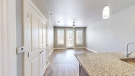This well-appointed one-bedroom, two-bathroom unit in Odessa, Texas, offers a thoughtfully designed single-floor layout that maximizes functionality and comfort. The kitchen serves as a standout centerpiece, showcasing rich dark-toned cabinetry, granite countertops, and a full suite of stainless steel Whirlpool appliances, including a range, over-the-range microwave, and a French door refrigerator. A peninsula with pendant lighting provides additional workspace and casual dining potential, all set atop warm wood-look flooring that extends through the main living areas. A clean hallway connects the kitchen and living spaces to the private quarters, maintaining a logical and efficient flow throughout. The bedroom is a comfortable retreat, carpeted for warmth and featuring dual windows dressed with white blinds that invite natural light and outdoor views. The primary bathroom connects directly to the bedroom and includes a granite-topped vanity with navy cabinetry, a bathtub with tiled surround, and wood-look flooring. A dedicated closet offers practical storage. Neutral wall tones, white baseboards, and consistent finishes throughout lend the space a cohesive, modern aesthetic well-suited for everyday living in West Texas.