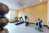 Located at 1601 E 121st Ave in Northglenn, Colorado, this exercise room delivers a comprehensive fitness facility within a compact, single-floor layout. The room features a clean, functional design with warm golden-yellow accent walls, crisp white ceilings, and smooth light-gray flooring that creates a bright and energizing atmosphere. Recessed lighting and a ceiling fan ensure the space remains well-lit and comfortable during workouts.

The cardio zone is anchored by two treadmills and an upright stationary bike, each equipped with digital display consoles. An elliptical-style machine rounds out the cardiovascular equipment selection. Natural light filters in through shuttered windows along one wall, adding an airy quality to the space.

A dedicated strength and functional training area houses a TAG-branded storage rack stocked with stability balls, medicine balls of varying weights, and kettlebells. A tiered dumbbell rack provides a full range of free weights alongside a workout bench, supporting a variety of strength training routines.

The room is accessed through a frosted-glass panel door and includes wall-mounted accessories for added convenience. Despite its modest footprint, the exercise room is thoughtfully organized to maximize usability, making it a well-appointed fitness amenity for residents or users of the property.