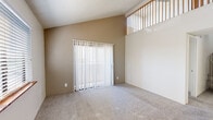 Located at 990 E River Rd in Tucson, Arizona, this residential unit offers a well-organized layout across a single floor with an impressive sense of vertical space. The living area is a standout feature, boasting dramatically vaulted ceilings with an open upper-level railing detail that adds architectural character and visual depth. A sliding glass door fitted with vertical blinds allows natural light to pour in while providing access to the outdoors. The textured ceiling and neutral-toned carpet complete the warm, inviting atmosphere of the main living space. The bedrooms are carpeted and simply appointed, each with windows fitted with blinds that allow for natural light and privacy. One bedroom includes an additional door providing convenient access. The kitchen is equipped with wood-trimmed cabinetry, speckled laminate countertops, a stainless steel sink, and black appliances including an electric range, dishwasher, and over-the-range microwave. Wood-look flooring adds a clean, durable finish to the kitchen area. The bathroom features wood-look tile flooring, a tub and shower combination with white tile surround, brushed nickel hardware and towel bars, and a clean, functional layout. Overall, the space presents a practical and comfortable living environment with notable architectural highlights.