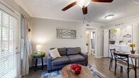 This thoughtfully designed one-bedroom, one-bathroom unit offers a warm farmhouse-inspired aesthetic across a single floor. The open-concept kitchen and living area serves as the heart of the space, featuring hardwood-style flooring, crown molding, and a textured ceiling with a ceiling fan overhead. The living room is anchored by a white brick fireplace and benefits from natural light streaming through a glass door with slatted blinds. The kitchen is equipped with granite-style countertops, white cabinetry, a dishwasher, and a full-size refrigerator, offering efficient use of space. The bedroom is a comfortable retreat with plush carpeting, a ceiling fan, and a window that allows natural light to fill the room. The bathroom features a single vanity with white cabinetry, a round mirror, and a shower-tub combination. A dedicated closet provides additional storage. Throughout the unit, neutral warm-toned walls and consistent hardwood-style flooring create a cohesive and inviting atmosphere. The farmhouse-inspired décor theme ties each room together, giving the space a distinct, homey character well-suited for comfortable single-occupant living.